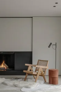 A minimalist interior design featuring a wooden armchair on a fur rug, a fireplace, and a modern floor lamp in a living room.