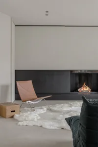 Minimalist living room with a leather chair and a fireplace, featuring a modern design aesthetic.