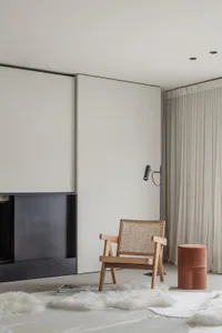 A minimalist living room with a wooden armchair, a floor lamp, and a white fur rug.