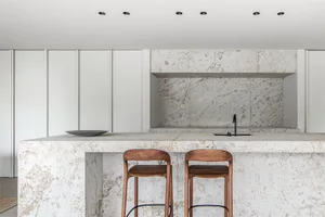 Modern minimalist residential kitchen with marble countertop and wooden stools.