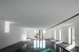 A minimalist indoor swimming pool with concrete walls and floor, large windows, and natural light.