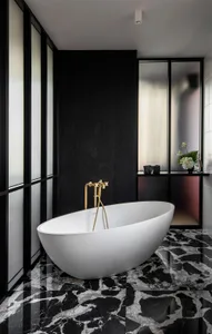A modern bathroom with a white oval bathtub, gold faucets, and a black and white marble floor.