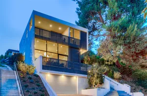 Modern house exterior made of glass, concrete, and wood in a hillside location.