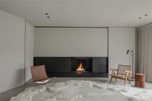 A modern, minimalist living room with a fireplace, sheepskin rug, and chairs.