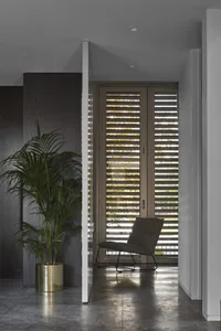 A hallway with a modern interior design featuring a metal floor, large planter with a plant, and a metal chair with a black c