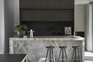 A modern kitchen featuring a marble counter top with stools and dark wood cabinets.