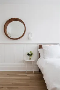 A minimalist bedroom featuring a bed with white bedding, a wooden headboard, and a small white side table with a vase of flow