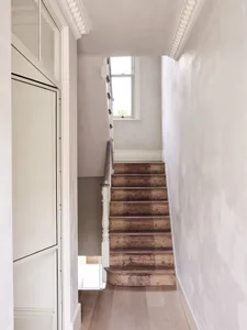 A minimalist white staircase with wooden steps and flooring, leading to a window.