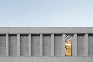 A modern building exterior with concrete pillars and a view into a well-lit interior space.