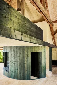 Circular wooden space with a dark wooden floor and a greenish staircase leading to a window.