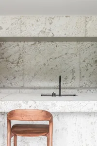 A modern kitchen featuring white marble countertops and a wooden chair.