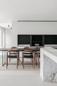 Contemporary residential kitchen featuring a sleek black-steel table surrounded by wooden chairs on a textured rug, with a mo