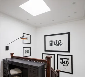 A modern home office featuring a black desk, white walls, and framed black and white photos on the wall.