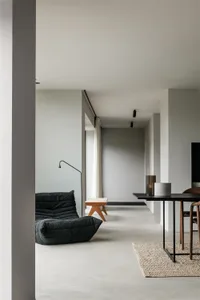 Contemporary living room with minimalist design featuring concrete flooring, minimalist furniture, and ambient lighting.