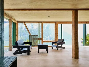 Modern minimalist living room with wooden furniture and large windows overlooking a scenic outdoor view.