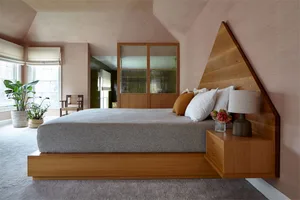 A modern bedroom featuring wood furniture, a bed with white and orange pillows, a floating nightstand with a lamp, and a pott
