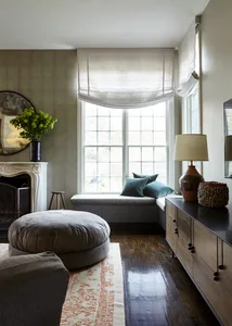 Modern living room with a fabric window seat, wooden cabinets, and a round ottoman on a patterned rug.