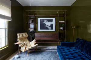 A modern living room with a blue tufted sofa, a white leather armchair, and metal shelves with brass accents.