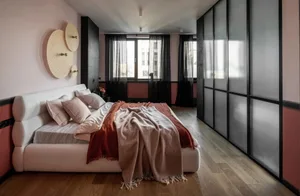 A modern bedroom with a white bed, pink and beige bedding, and wood flooring.