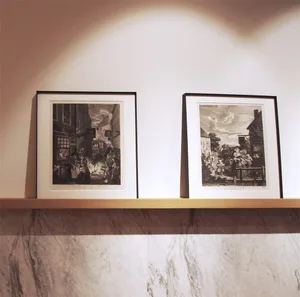 Two framed black and white artworks on a white background, one depicting a busy street scene with people and buildings, the o