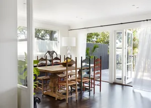 A minimalist dining room with wooden furniture, large windows, and a relaxed atmosphere.