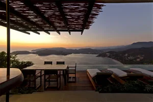 現代簡約露台，木質平台搭配玻璃桌椅，俯瞰日落海景。