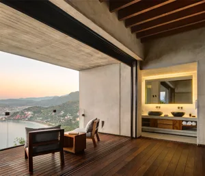 A modern bathroom with concrete walls and a large window overlooking the ocean.