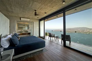 A modern bedroom featuring a wooden floor and glass windows overlooking a scenic view.