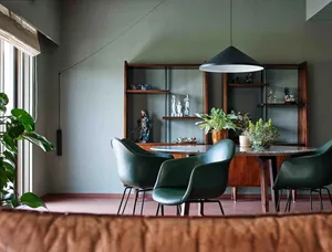 A modern dining room featuring green leather chairs and a round dining table with decorative plants and sculptures.