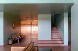 A modern interior with a large window, a leather couch, a wooden bench, and a metallic door.