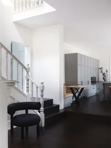 Modern kitchen and dining area with wooden flooring, black chair, and grey cabinets.