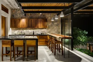 Contemporary residential kitchen with wooden cabinets and countertops, stone backsplash, and seating area.