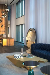 A modern living room featuring a metal and wood coffee table, a navy blue tufted sofa, and white curtains.