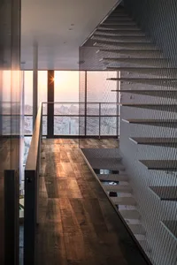 Modern staircase featuring metal and glass railings with a cityscape view at sunset.