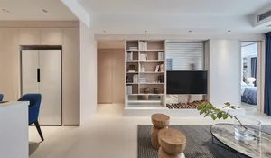 A modern minimalist living room with neutral tones, featuring a bookshelf, television, and seating area.