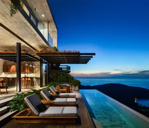 A modern residential home with wooden and glass features, overlooking a serene ocean view.