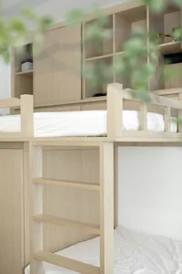 A minimalist bunk bed with wooden construction and white bedding, featuring a wooden ladder.