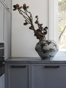 A minimalist ceramic vase containing dried plant branches on a sleek, modern kitchen countertop.