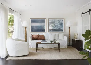 A minimalist living room with white furniture, a glass coffee table, and metal floor lamps.