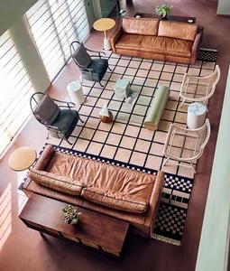 A modern living room featuring two brown leather sofas, a checkered rug, and diverse seating options including armchairs and 