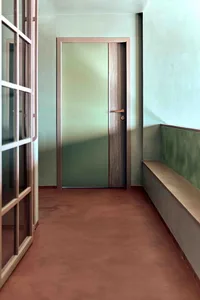An image of a minimalist corridor with a concrete floor and walls, featuring a door with a wooden frame and a bench along the