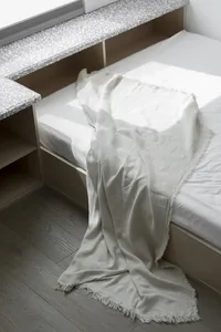 A minimalistic bedroom with a cotton-blend blanket draped over the bed.