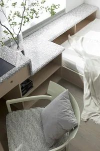 A minimalist bedroom with a white bed, terrazzo desk, and wooden elements.