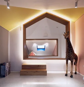 A modern living room with a wooden ceiling and walls, featuring a giraffe toy and a window with a small bedroom in the backgr