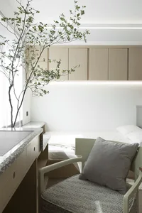 A minimalist bedroom featuring a fabric chair with a cushion, modern furniture, and a green plant.