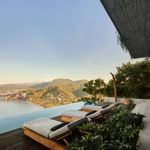 A modern poolside lounge area featuring concrete and wooden furniture overlooking a scenic landscape.