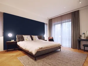 A modern minimalist bedroom featuring neutral-colored furniture and a dark headboard wall.