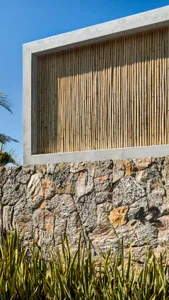 A modern exterior wall made of concrete and stone with a bamboo screen.