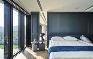 Modern minimalist bedroom featuring a textured panel wall and a large window overlooking the natural landscape.