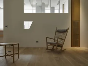 A minimalist home interior featuring a wooden floor, a rocking chair, a wooden coffee table, and a wooden column.